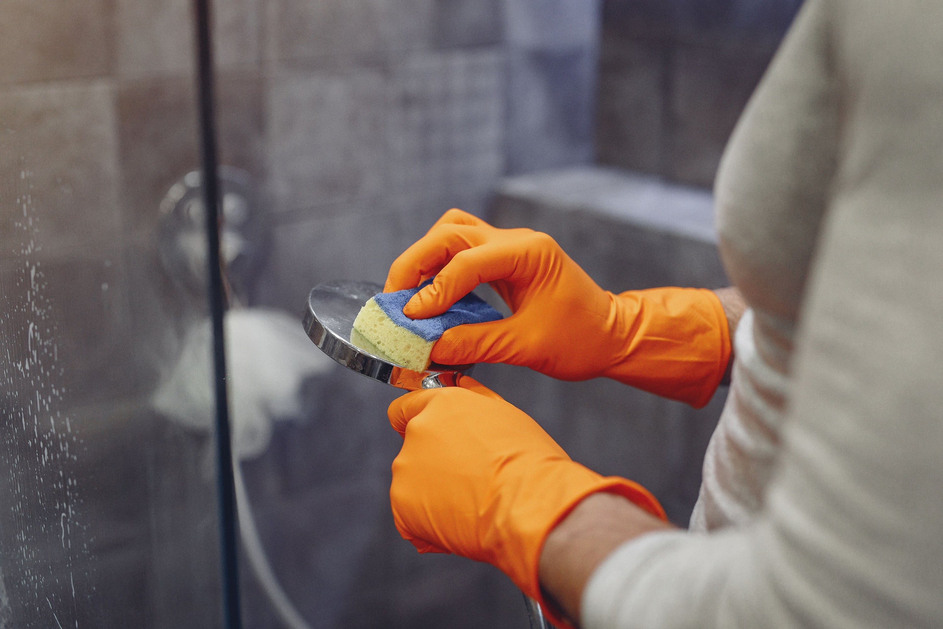Person using a small brush to clean shower door tracks in a bright bathroom